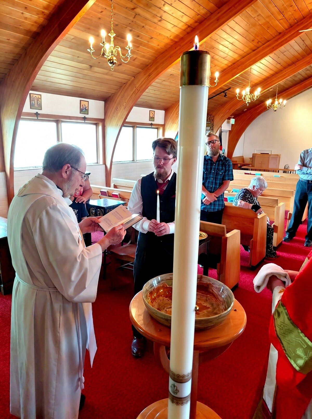 The newly baptized holds his lit baptismal candle beside the tall Paschal candle